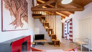 A modern living room with a wooden staircase, a large tree mural, and a red entertainment unit. - Nice apartment for 3 guests with WIFI, TV, patio and pets allowed (Mondovì)