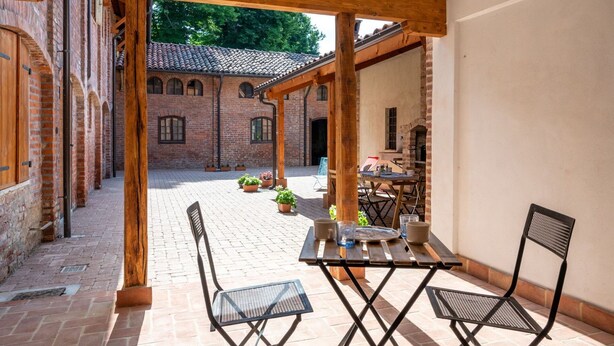 A courtyard with a brick building, wooden pergola, and a table with chairs. - Nice apartment for 3 guests with WIFI, TV, patio and pets allowed (Mondovì)