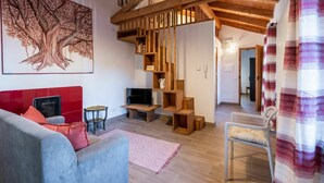A modern living room with a red accent wall, a large tree mural, wooden shelving, a TV, and a staircase leading to another room. - Nice apartment for 3 guests with WIFI, TV, patio and pets allowed (Mondovì)