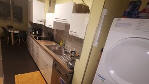 Een kleine keuken met een vaatwasser, een spoelbak en kastjes. Er is een eethoek met een tafel en stoelen.