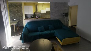 Een woonkamer met een blauwgroene bank, een gele salontafel en een accentmuur van steen.