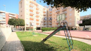A playground with slides and a basketball court, surrounded by a residential building with balconies. - 035 - Gaviotas 002 - comfortHOLIDAYS (Santa Pola)