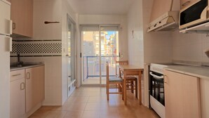 A compact kitchen with a dining area, a view through the glass door, and a microwave above the stove. - 035 - Gaviotas 002 - comfortHOLIDAYS (Santa Pola)