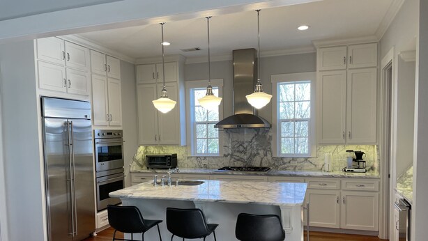 A modern kitchen with white cabinetry, a stainless steel refrigerator, a built-in oven, a gas stove, and a marble island with bar stools.