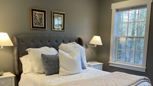 A bedroom with a large bed, two bedside tables, a window with a view, and two wall-mounted lamps.