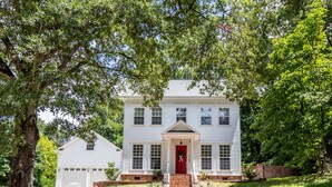 A two-story white house with a red front door, brick steps, and a garage.