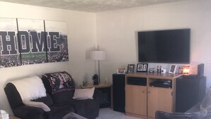 A living room with a large flat-screen TV, a sofa, a coffee table, and a lamp. - Your Penn State Destination (State College)