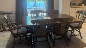 A dining area with a wooden table and chairs, a ceiling fan, and a view of the outdoors through large windows. - Your Penn State Destination (State College)