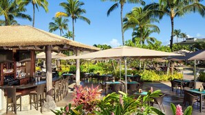 An outdoor bar area with tables and chairs, surrounded by tropical plants and palm trees.