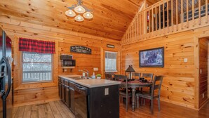 A wooden cabin interior with a kitchen, dining area, and a loft bedroom.
