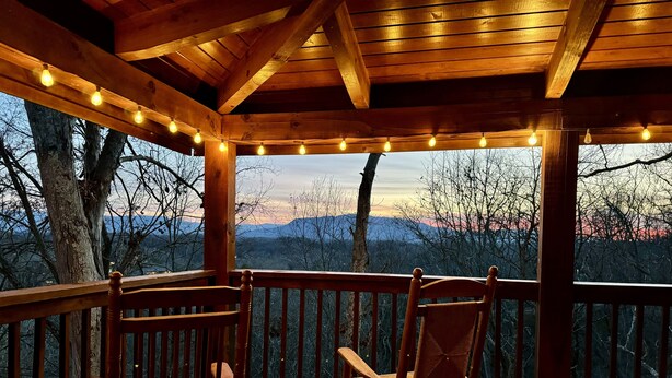 A wooden deck with two rocking chairs and string lights, overlooking a mountainous landscape.