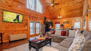 A cozy cabin interior with a wooden interior, a large TV mounted on the wall, a dining area, and a comfortable seating arrangement.