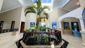 Un vestíbulo amplio con techo alto, una palmera en el centro y obras de arte en las paredes.