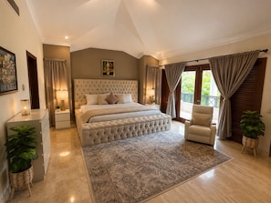 Une chambre à coucher avec un grand lit, une chaise, une table de chevet, une commode et une fenêtre avec des rideaux.