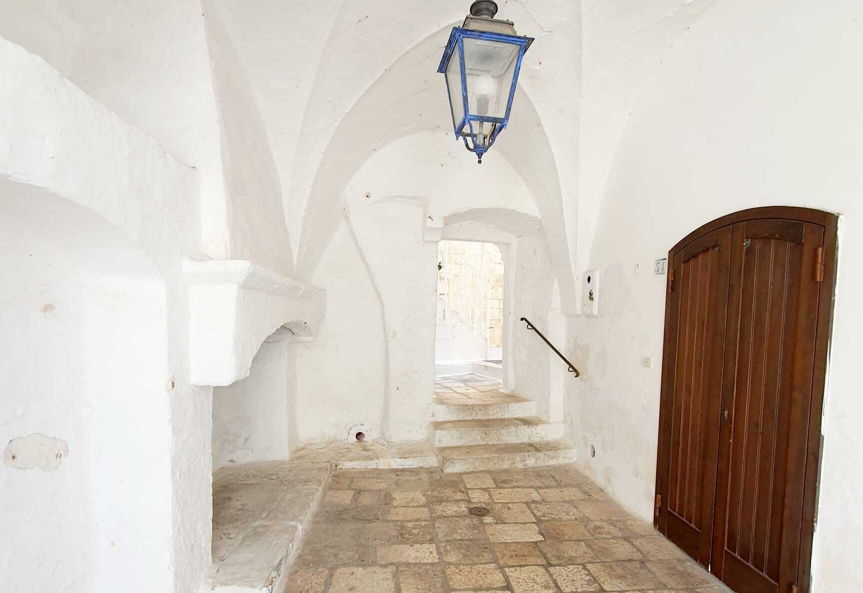 A narrow hallway with white walls, a wooden door, and a stone floor.