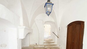 Un pasillo estrecho con paredes blancas, una puerta de madera y suelo de piedra.