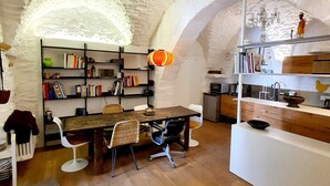 Una habitación rústica con una mesa de madera, sillas, una estantería y una zona de cocina.