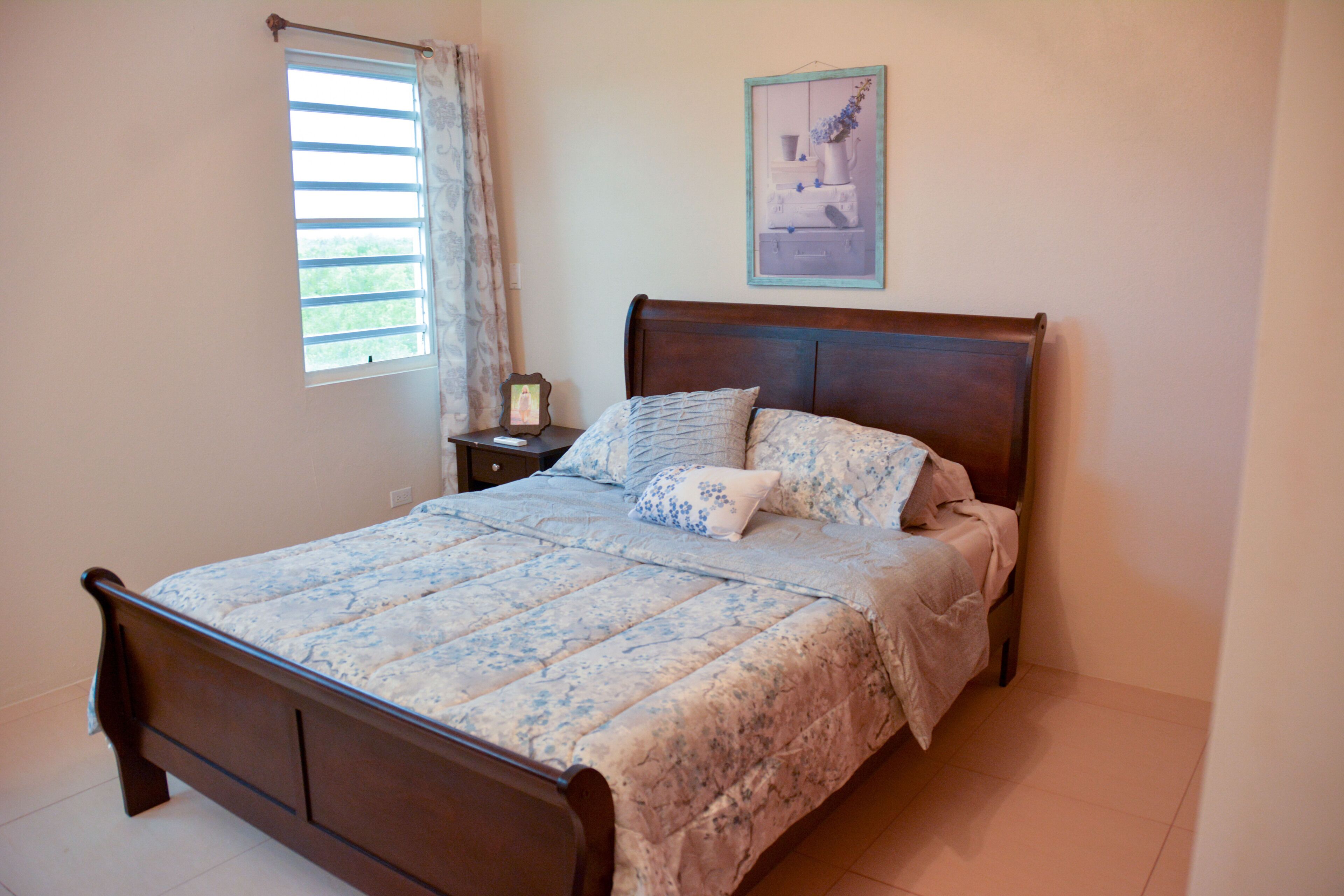 A bedroom with a wooden bed, a bedside table with a lamp, and a window with curtains.