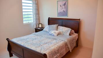 A bedroom with a wooden bed, a bedside table with a lamp, and a window with curtains.