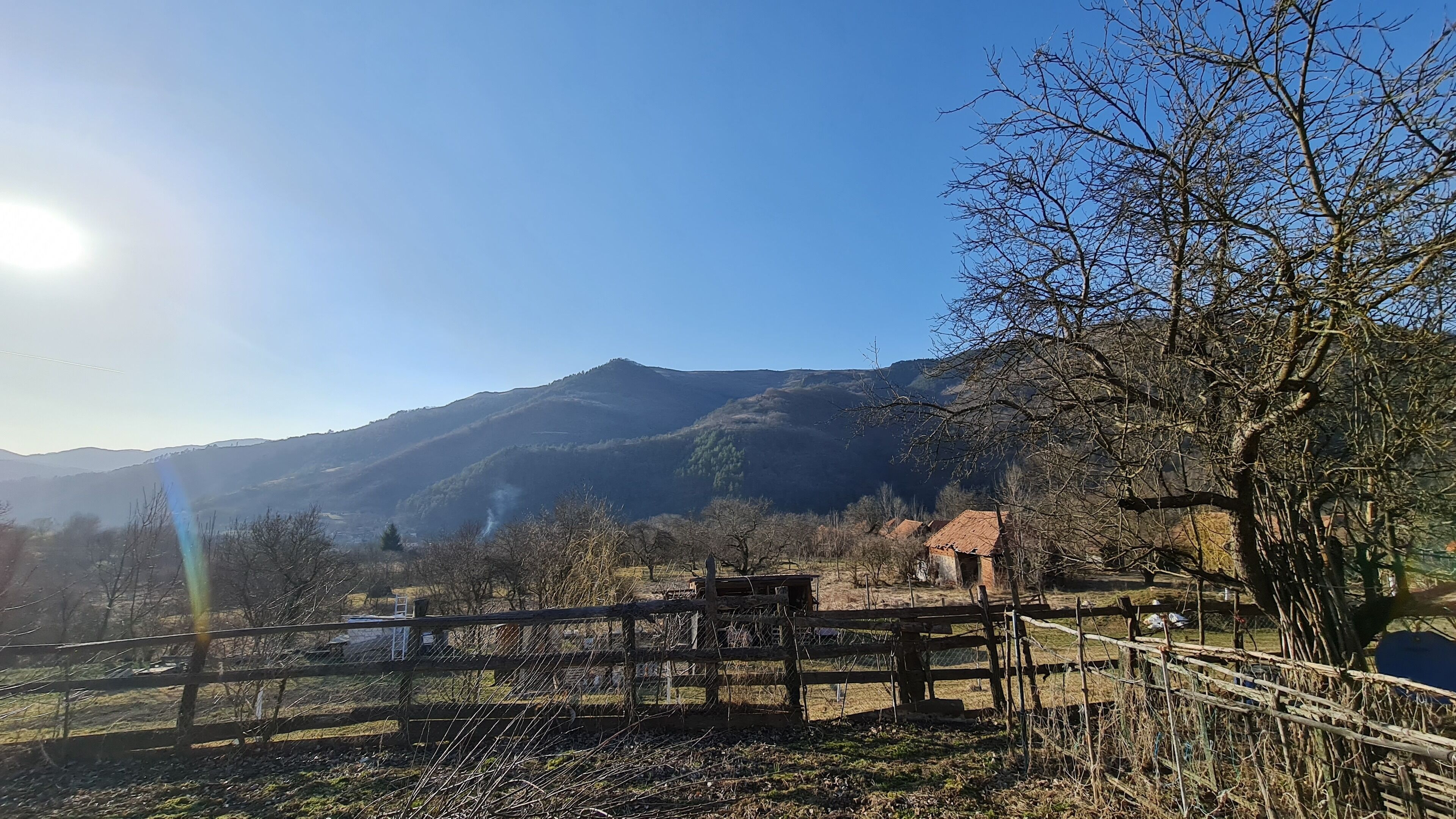 A rural landscape with a wooden fence, a small building, and mountains in the background.