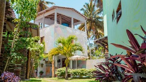 A two-story building with a covered patio and a garden with palm trees and plants.