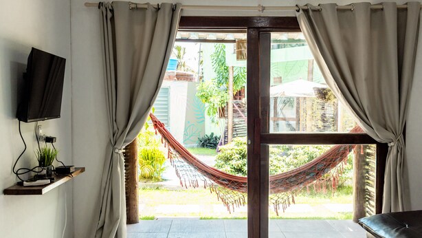 A room with a TV on a shelf, a hammock outside, and a view of greenery.