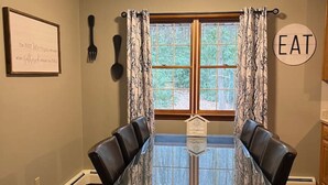A dining room with a glass-top table, black leather chairs, a window with curtains, a wall-mounted sign that says "EAT", and a framed certificate on the wall. - 8 bed Lodge Near Camelback/Outlets-HOT TUB (Tannersville)