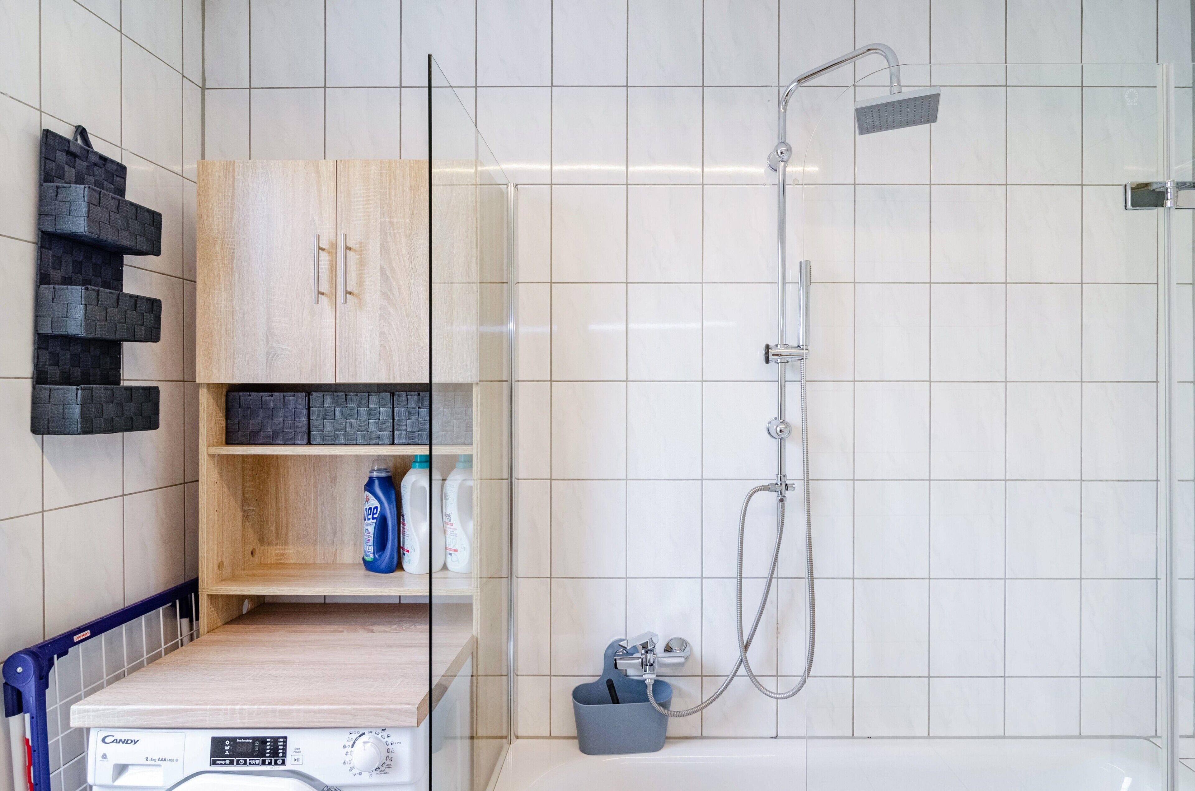 Een moderne badkamer met een douche, een houten kast met planken en een wasmachine.