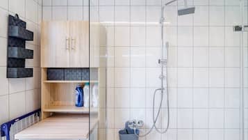 Een moderne badkamer met een douche, een houten kast met planken en een wasmachine.