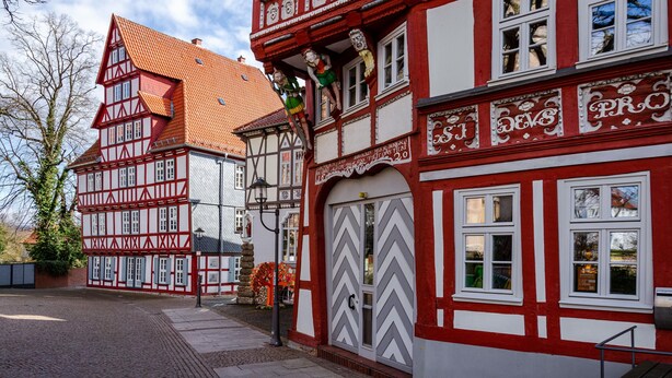 Un edificio tradicional de entramado de madera con fachada roja y blanca, un escaparate visible y una calle empedrada.