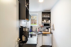 A compact kitchen with a microwave, toaster, sink, and a window with a view of trees. - Apartment 'West-Östlichen Tor' with Landmark View & Wi-Fi (Ecklingerode)