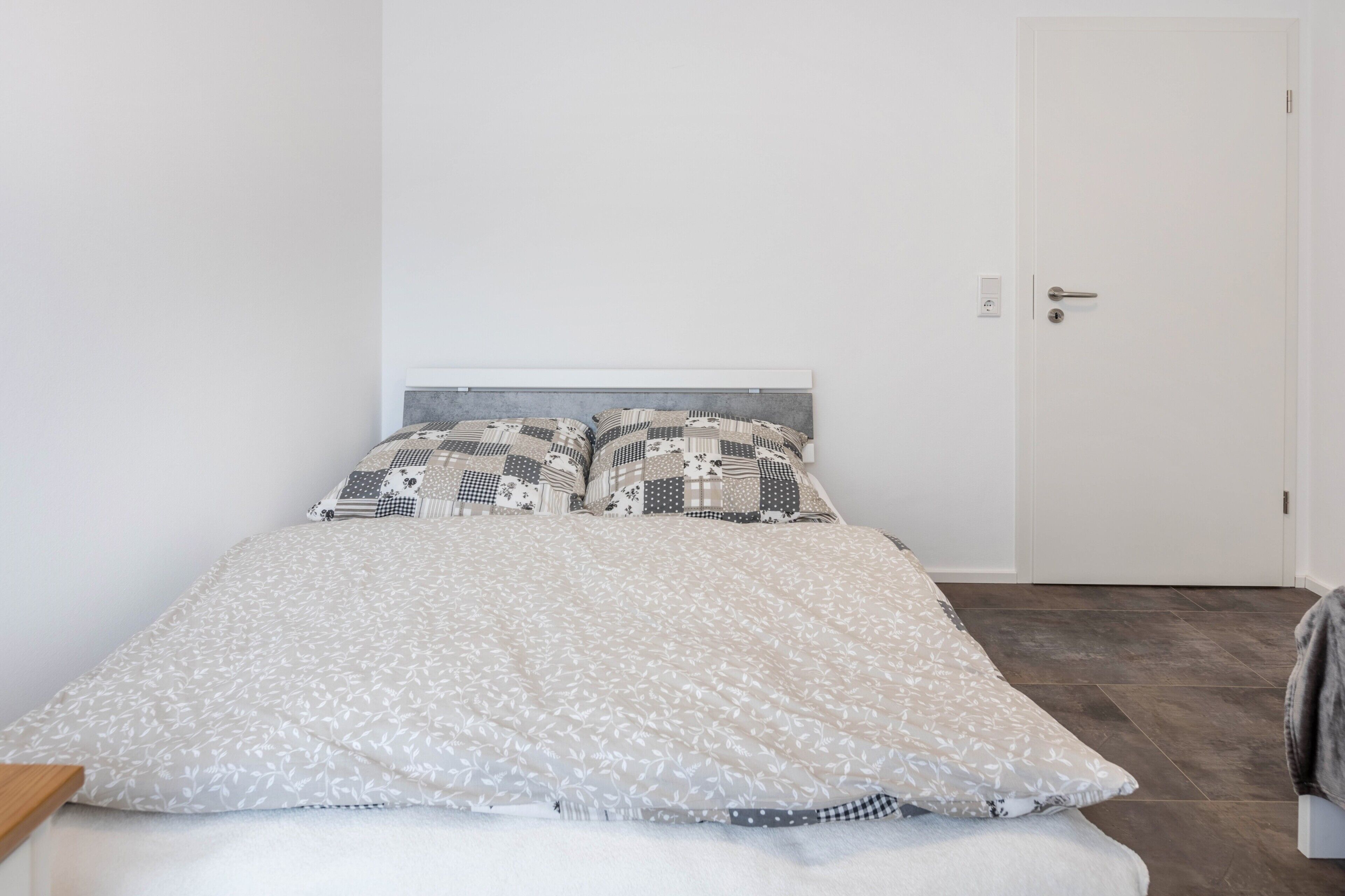 A bed with patterned bedding, a white headboard, and a door to the right.