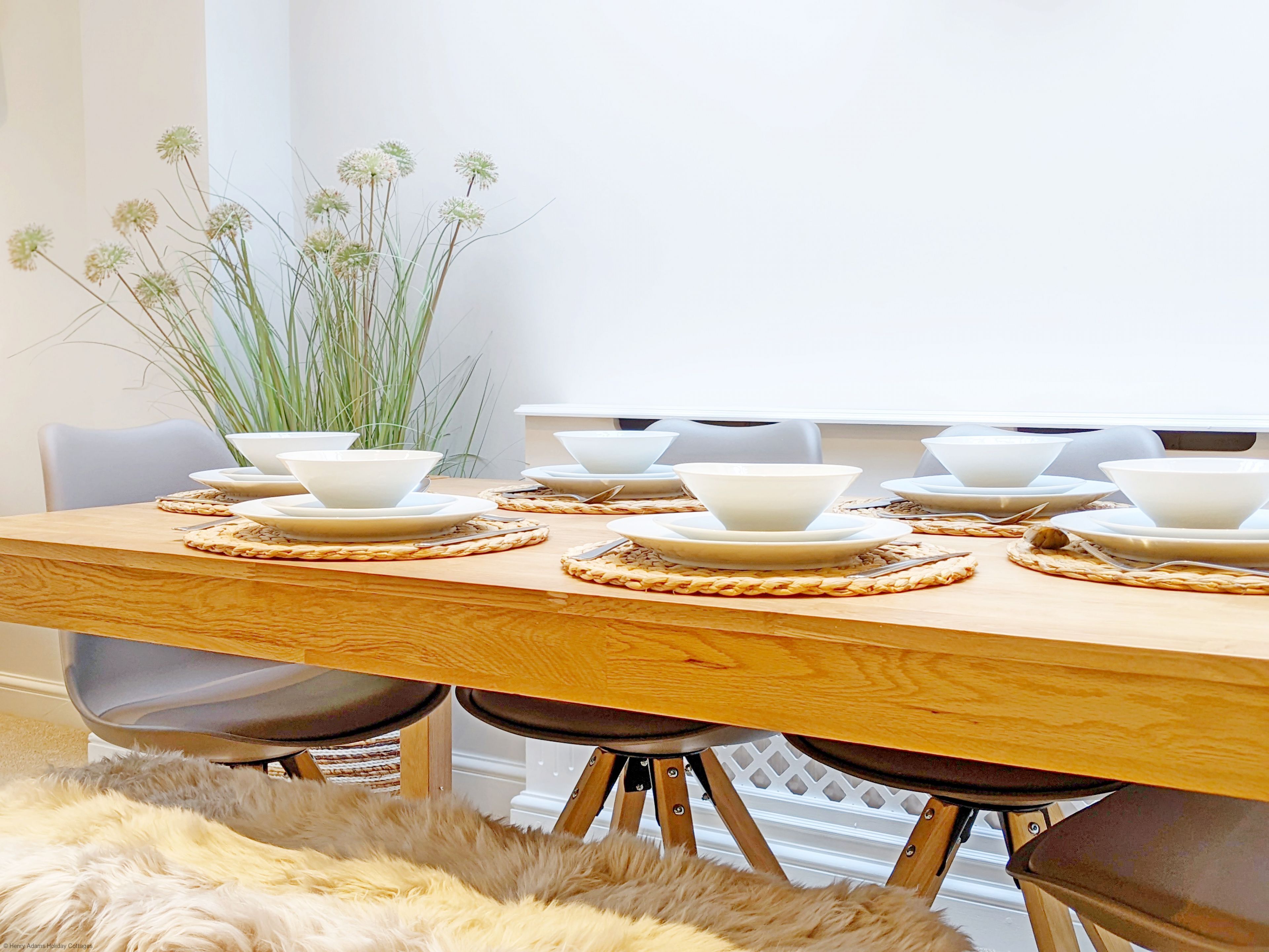 A dining table set with white bowls and plates, surrounded by chairs, with a plant in the background.