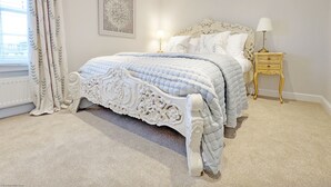 Un dormitorio con una cama grande, un cabecero decorativo, una mesita de noche con lámpara y una ventana con cortinas.