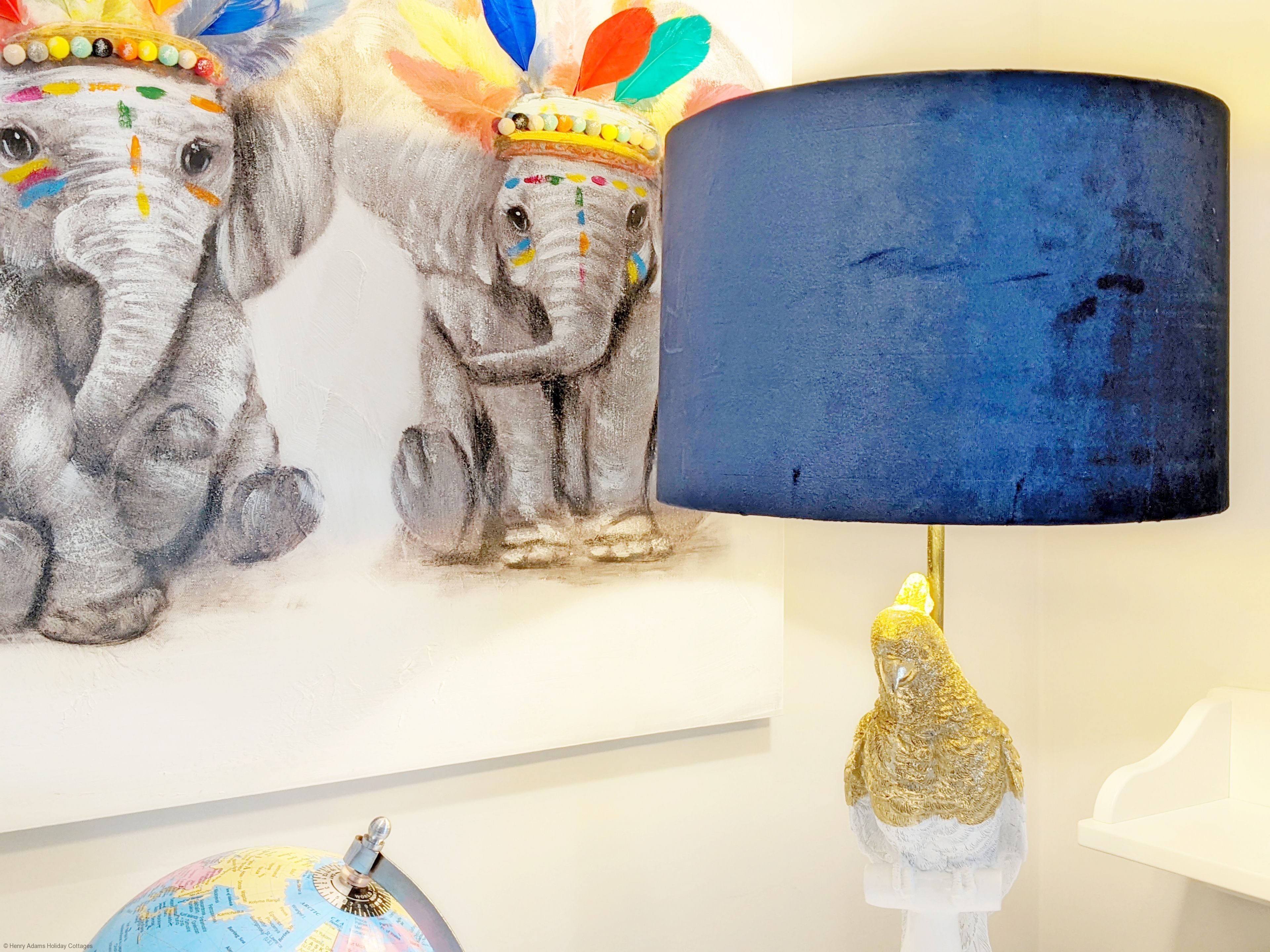 A room with a blue lamp, a globe, and a painting of elephants.