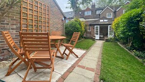 Eine Terrasse mit Holzmöbeln, einer Ziegelmauer und einem Gartenweg, der zu einem Haus führt.