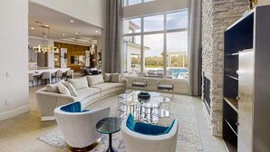 A spacious living area with a large window, a modern fireplace, and a dining area with a glass table. - Luxurious Oasis with Immersive Circus Bedroom at Reunion (Kissimmee)