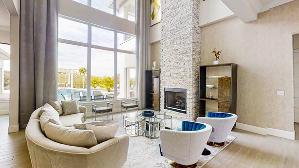 A spacious living room with a stone fireplace, modern furniture, and large windows offering a view of the outdoors. - Luxurious Oasis with Immersive Circus Bedroom at Reunion (Kissimmee)