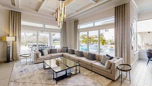 A spacious living room with a large sectional sofa, a glass coffee table, and a view of an outdoor swimming pool. - Luxurious Oasis with Immersive Circus Bedroom at Reunion (Kissimmee)