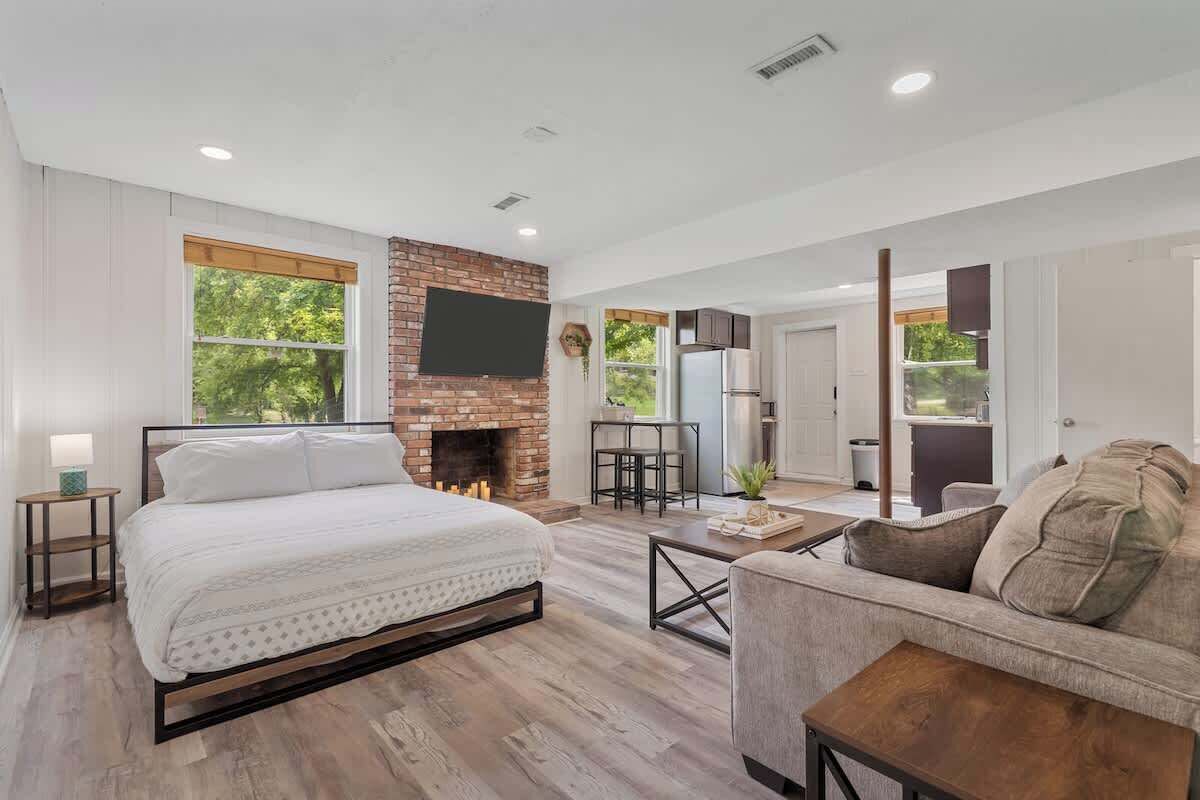 A modern bedroom with a brick fireplace, a large bed, and a view of the outdoors.