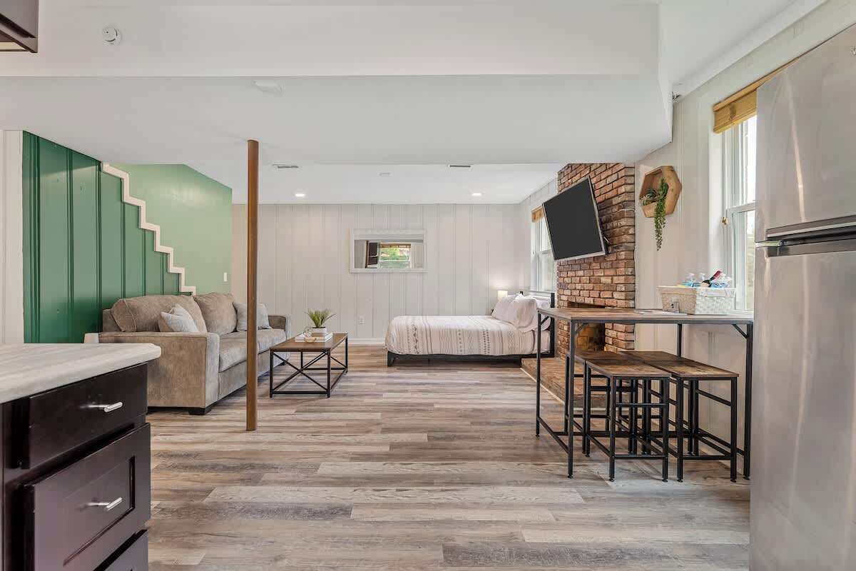 A modern interior with a kitchen area, a dining table with benches, a sofa, and a staircase.