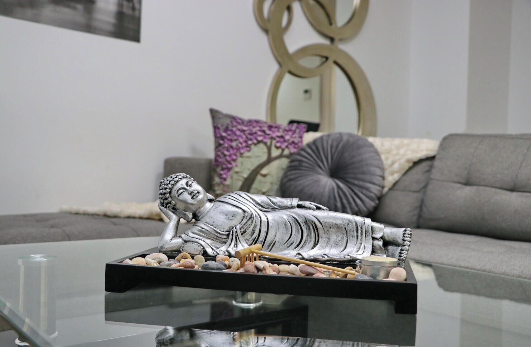 Una estatua de Buda sobre una mesa de cristal, con una bandeja de piedras y un bastón.