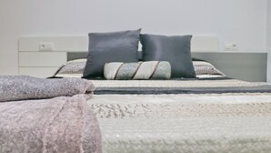 Una cama con cabecera blanca, almohadas grises y blancas, y una manta gris.