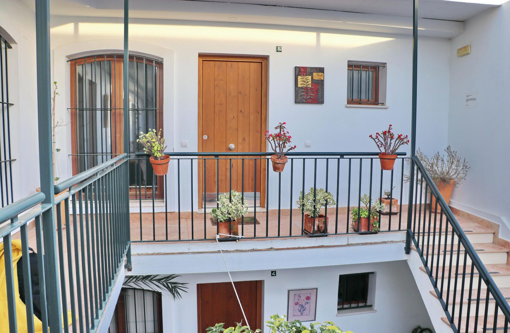 Un edificio residencial de varios niveles con balcón, plantas en macetas y una puerta de madera.