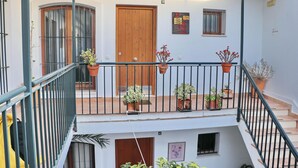 Un edificio residencial de varios niveles con balcón, plantas en macetas y una puerta de madera.