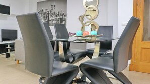 Un comedor moderno con una mesa de vidrio rodeada de sillas negras. Se ve una pieza decorativa y una pintura de la ciudad al fondo.