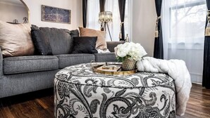 A modern living room with a grey sofa, patterned ottoman, and decorative items. - Roaring Riverside - Art Deco Luxe - 2 Kings! (Wichita)