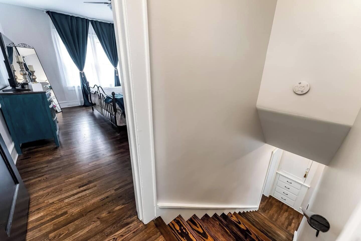 Un interior moderno con suelo de madera, pared blanca y zona de cocina con encimera azul y un espejo.