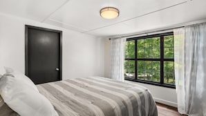 A bedroom with a bed, a window with curtains, a door, and a ceiling light. - Pleasure Point Place WATERFRONT Cottage (Florien)