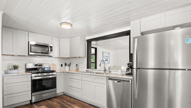 A modern kitchen with white cabinetry, stainless steel appliances, and a wooden floor. - Pleasure Point Place WATERFRONT Cottage (Florien)